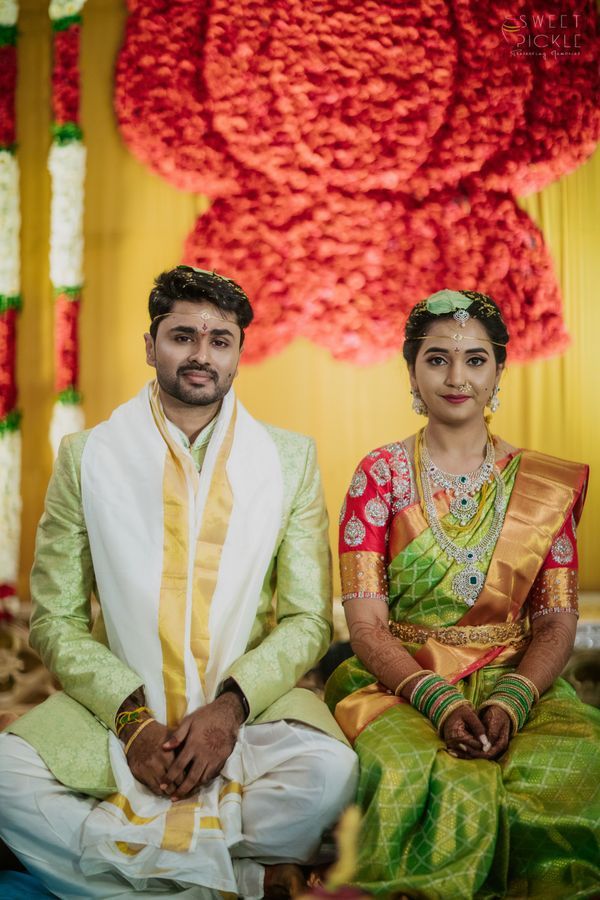 Traditional Telugu wedding couple in elegant green and red attire, captured beautifully during ceremony with floral backdrop — best wedding photographers in Hyderabad.